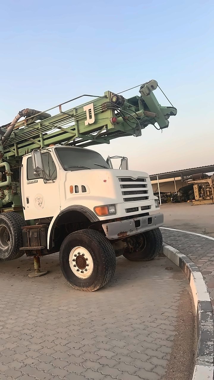 Drilling rig with a green mast on a white truck